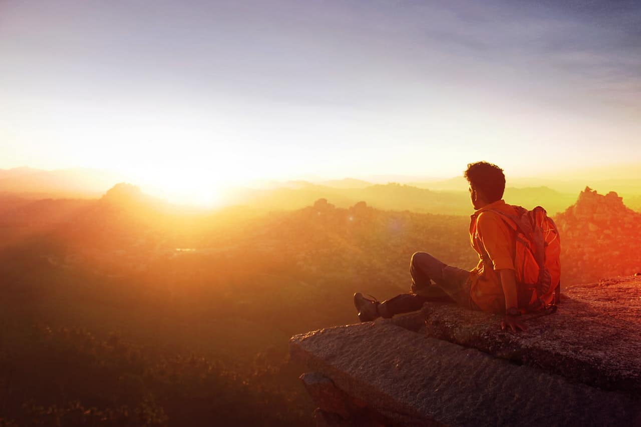 man-sitting-on-edge-facing-sunrise