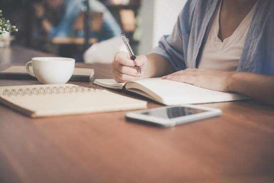 woman-writing-on-a-notebook-beside-teacup-and-tablet